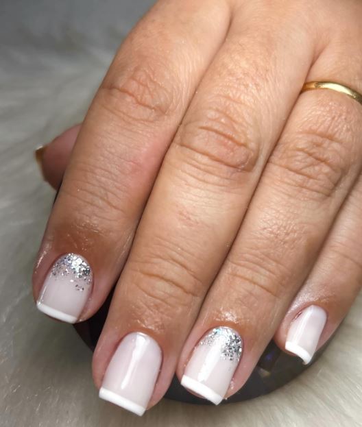 Unhas brancas decoradas com pedraria e brilho.